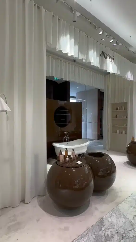 Amoue Pop-up Stand Bijenkorf Amsterdam 6 Geplooide ecru gordijnen naast de ronde presentatiemeubels van Amoué